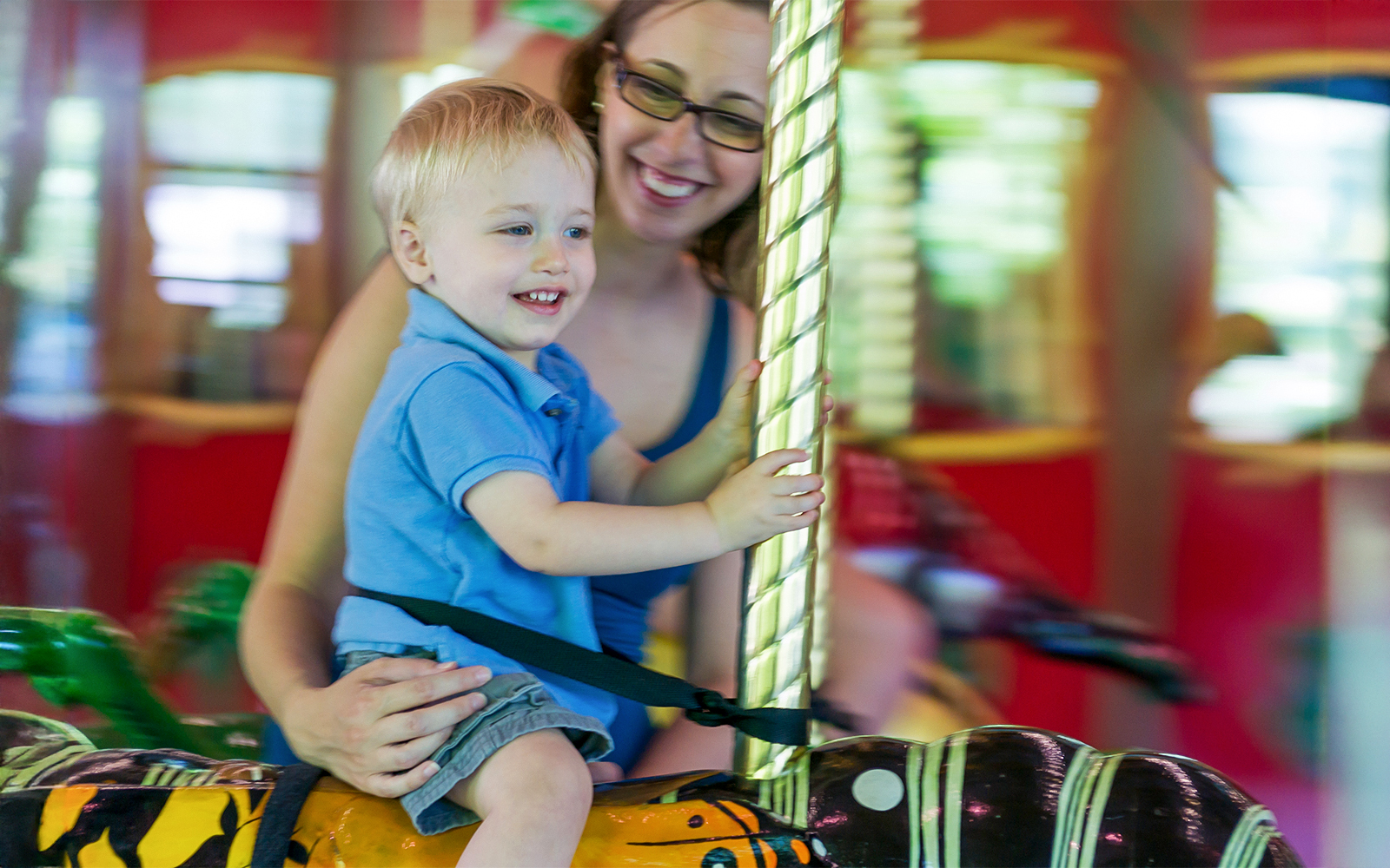 Child riding a carousel horse with an adult at an amusement park.