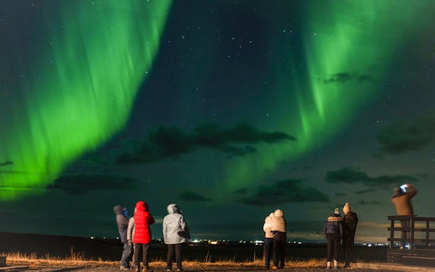 Small group watching Northern Lights on off-road tour with hot chocolate.