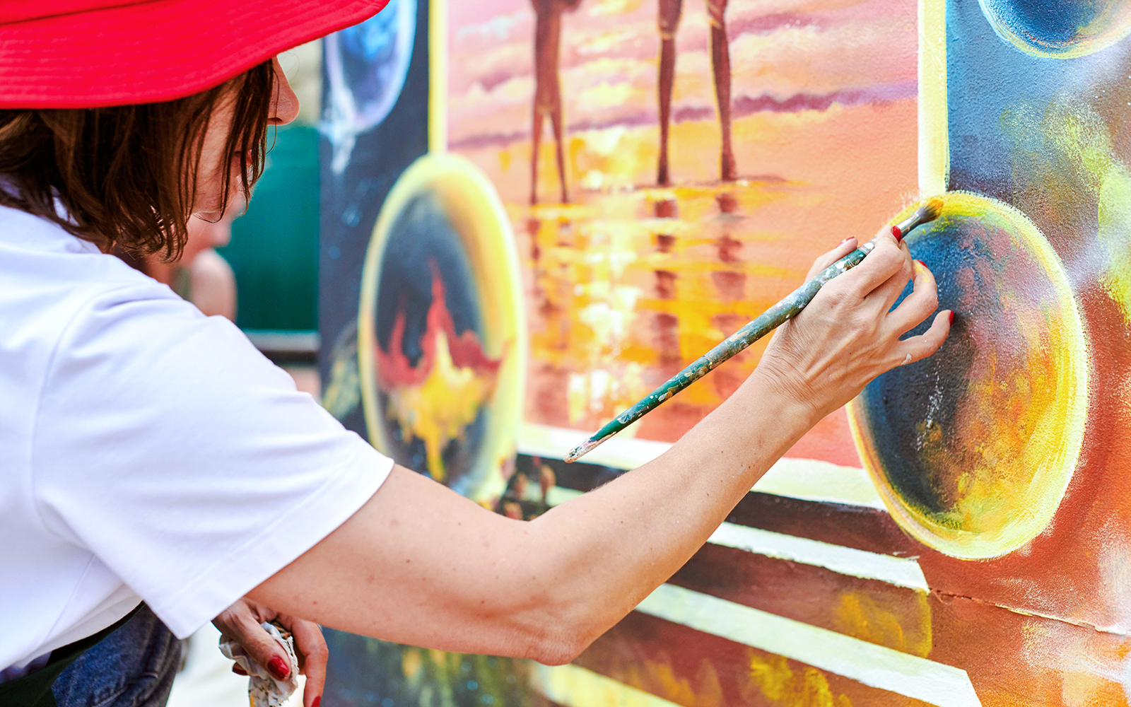Female artist in red hat painting colorful mural with brush.
