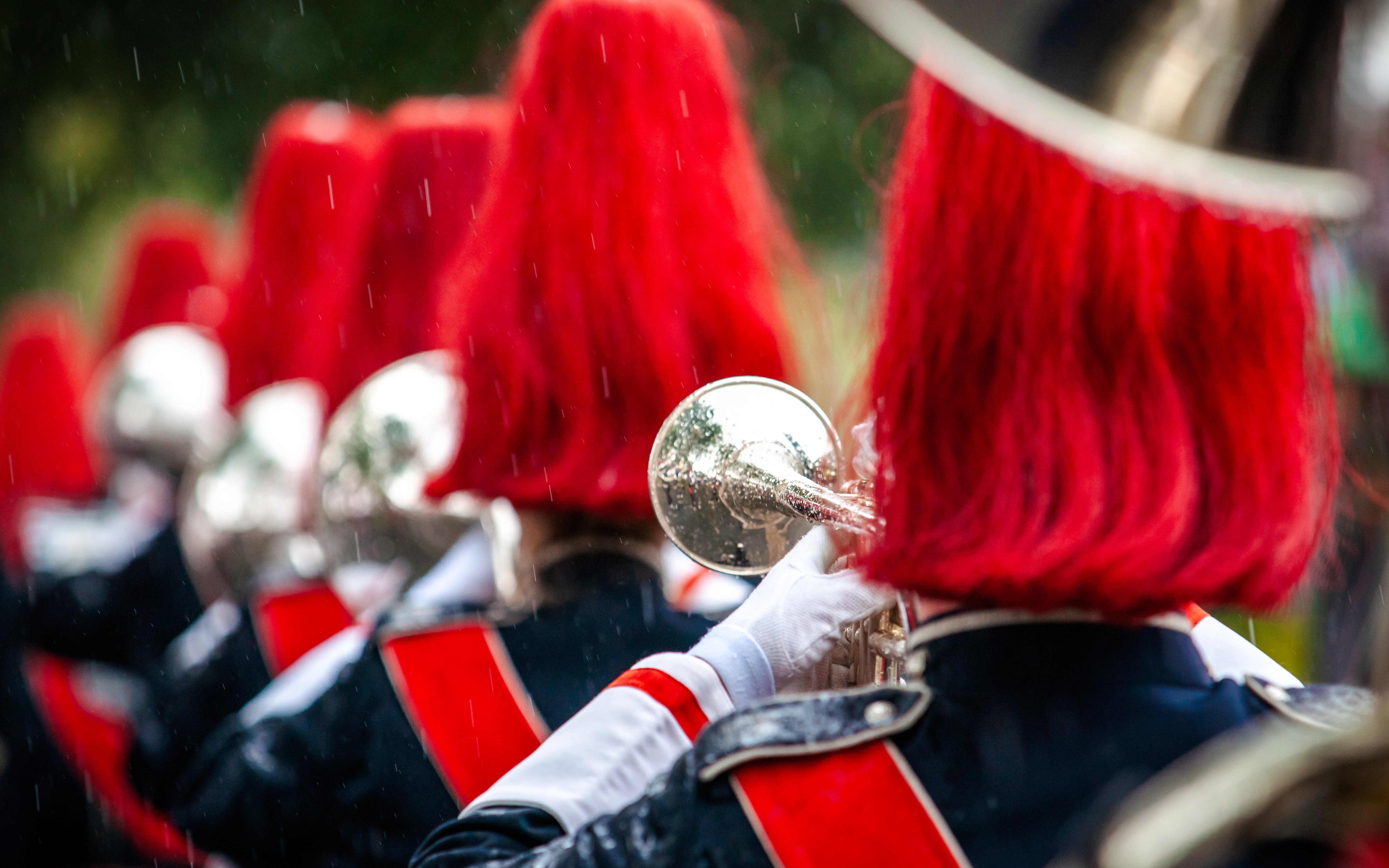 Marching band in red uniforms playing brass instruments in formation.
