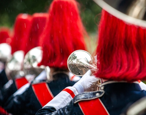 Marching band in red uniforms playing brass instruments in formation.