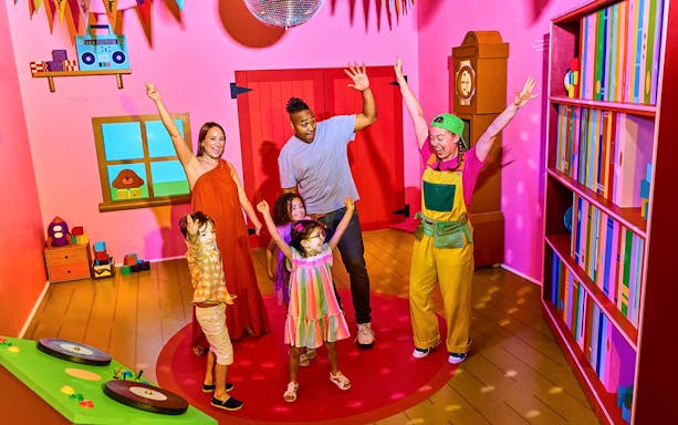 Children and adults enjoying CBeebies Rainbow Adventure in a colorful playroom.