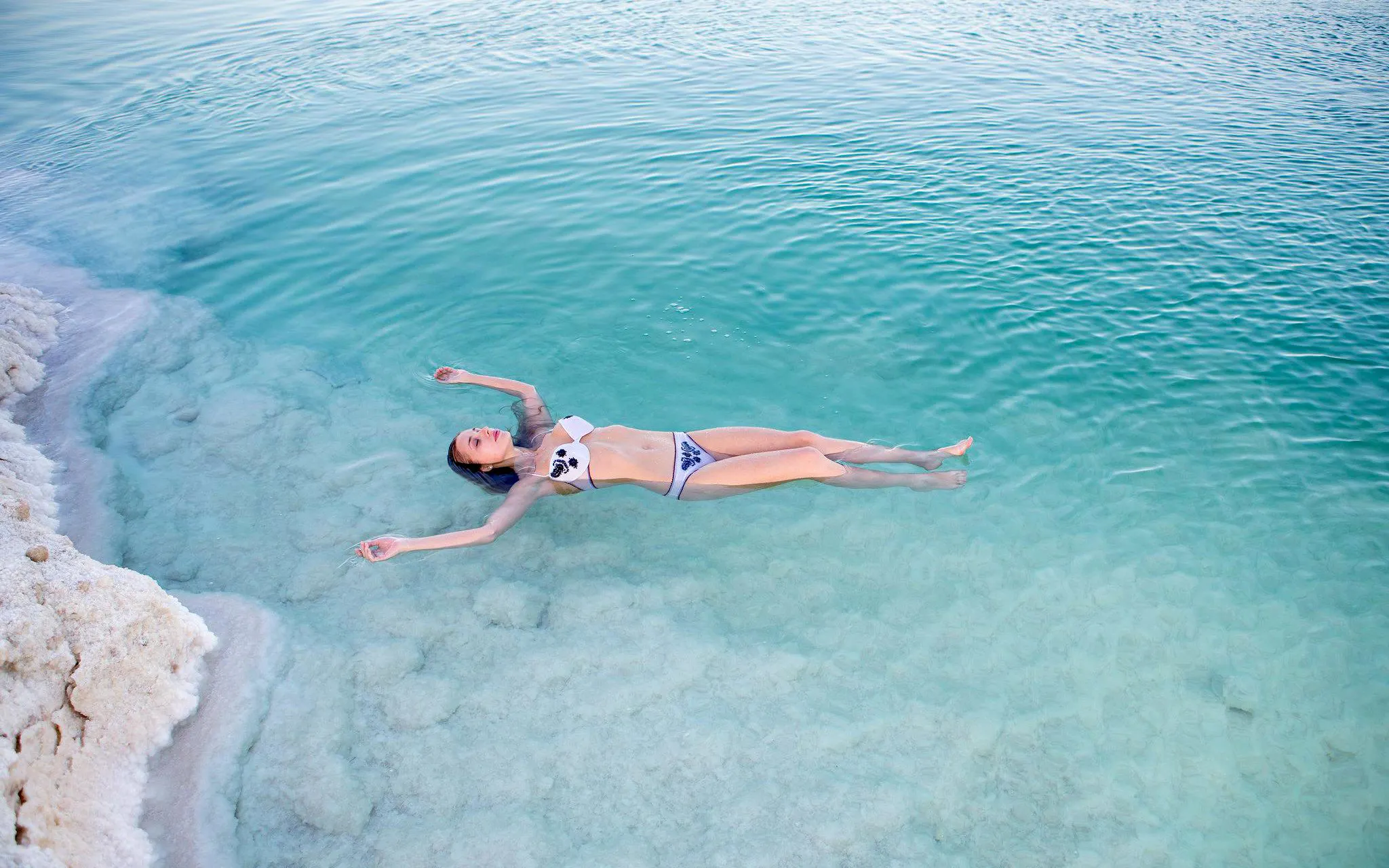 Person floating in the Dead Sea near salt formations, part of a tour from Amman to Petra, Wadi Rum, and Dead Sea.