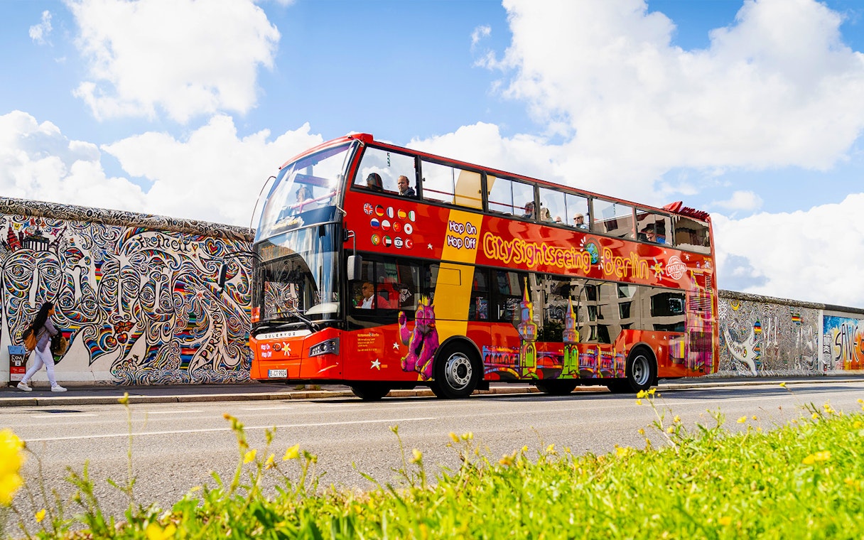 Red double-decker bus on Berlin Hop On & Hop Off tour passing the East Side Gallery.