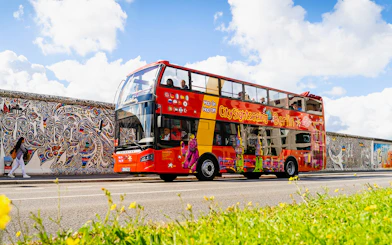 Red double-decker bus on Berlin Hop On & Hop Off tour passing the East Side Gallery.