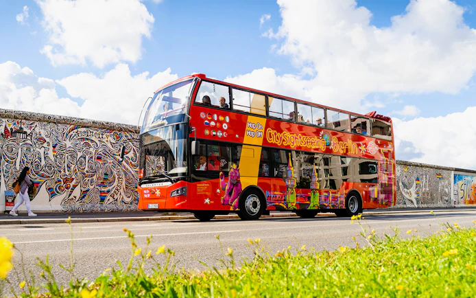 Red double-decker bus on Berlin Hop On & Hop Off tour passing the East Side Gallery.