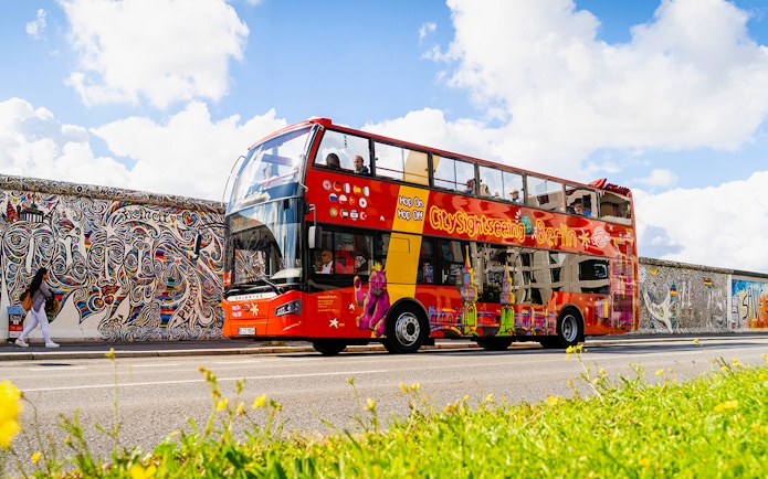 Red double-decker bus on Berlin Hop On & Hop Off tour passing the East Side Gallery.