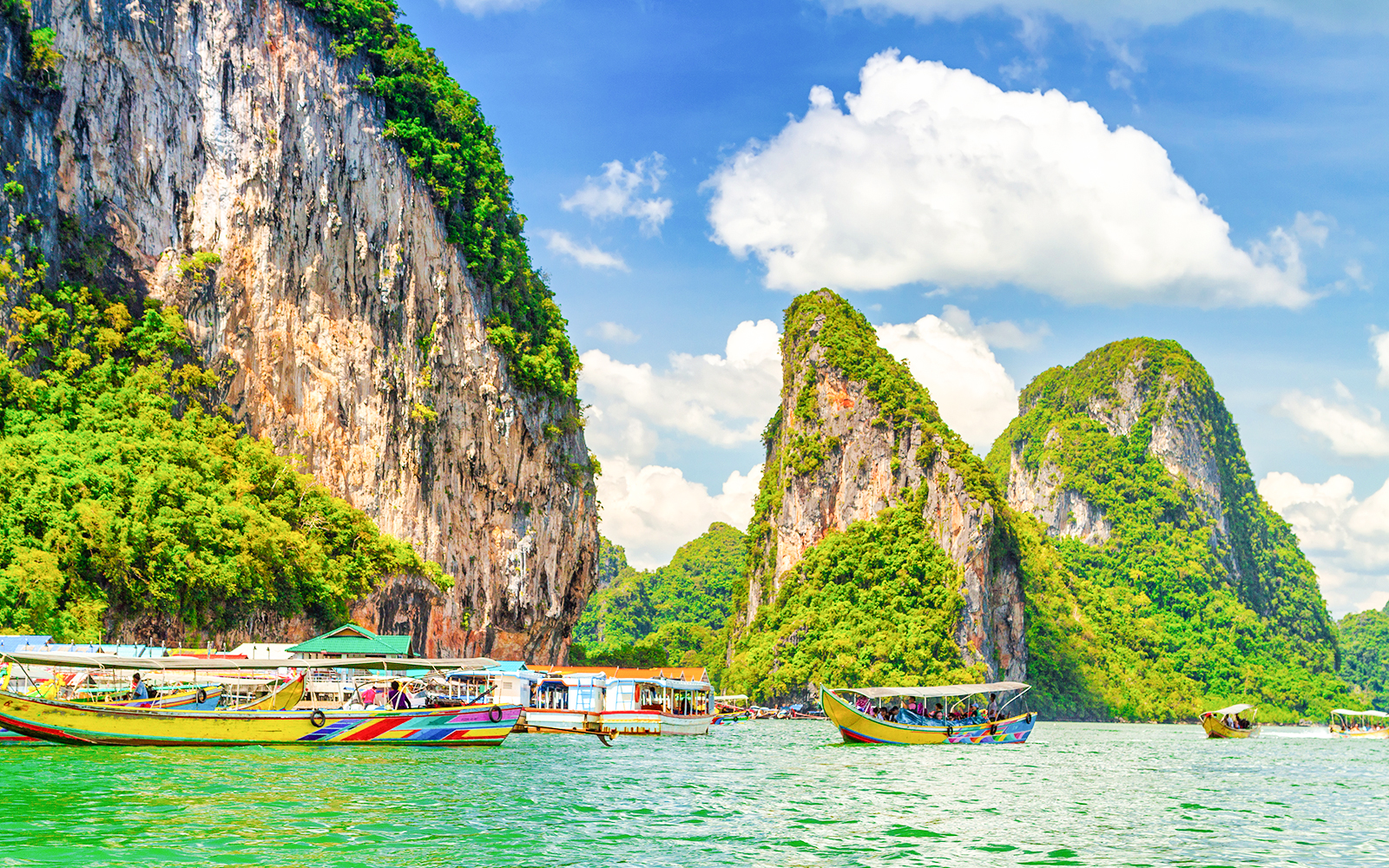 Boats on turquoise water with limestone cliffs in Koh Panyee, Thailand.