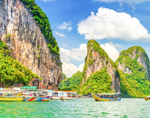 Boats on turquoise water with limestone cliffs in Koh Panyee, Thailand.