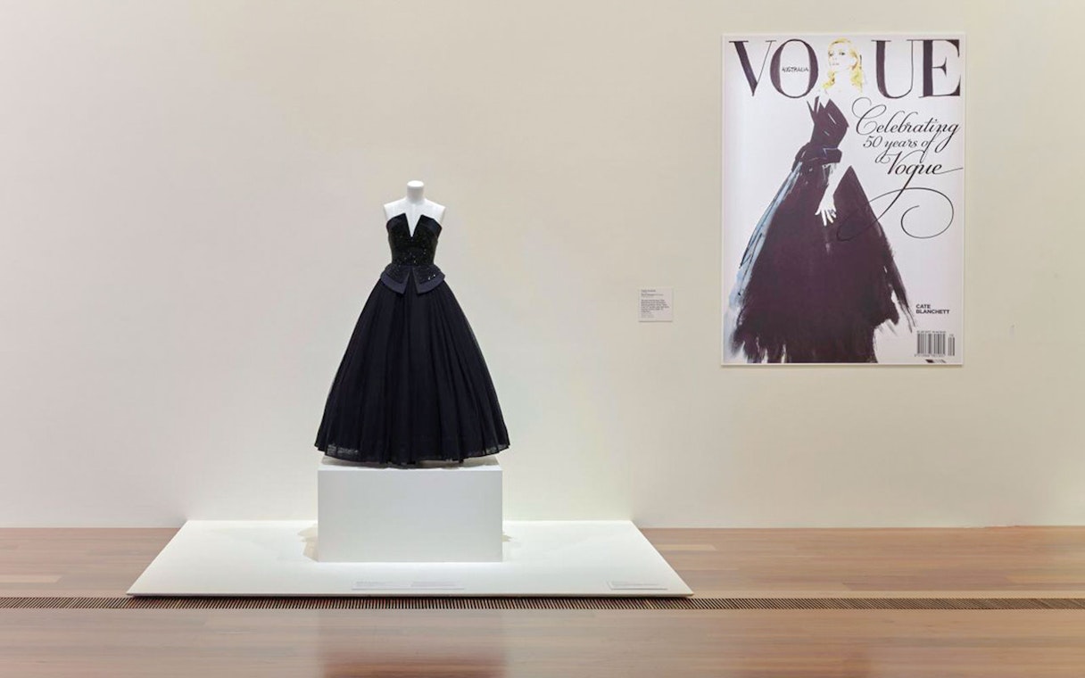 Mannequin displaying a black gown at Martin Grant Exhibition with Vogue cover in background.