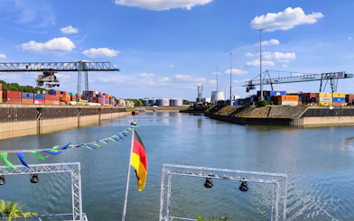 Cologne Harbour with cranes and shipping containers along the waterway.