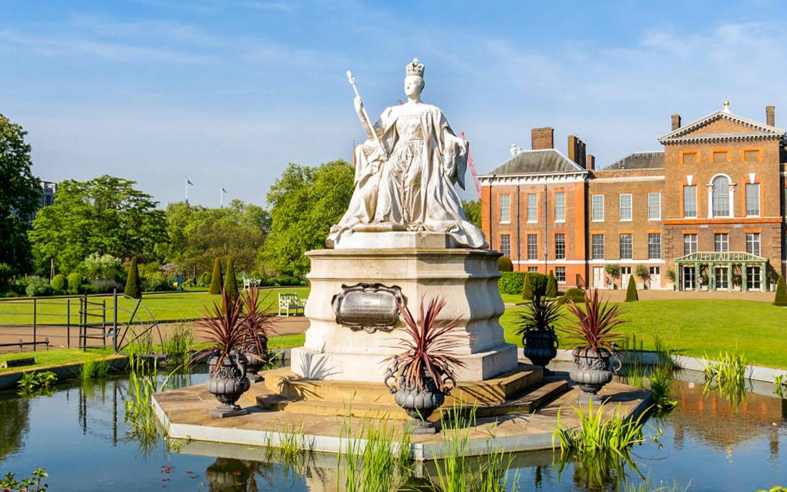 Queen Victoria Statue in front of Kensington Palace, London, surrounded by gardens.