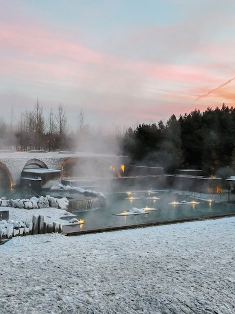 Laugarás Lagoon with steaming hot springs and snow-covered landscape at sunset.