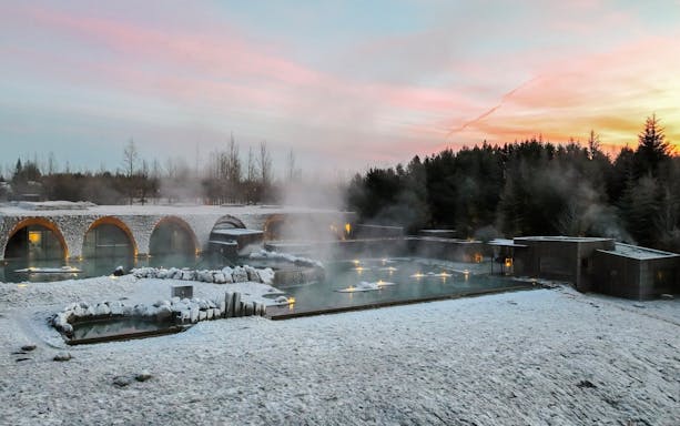 Laugarás Lagoon with steaming hot springs and snow-covered landscape at sunset.