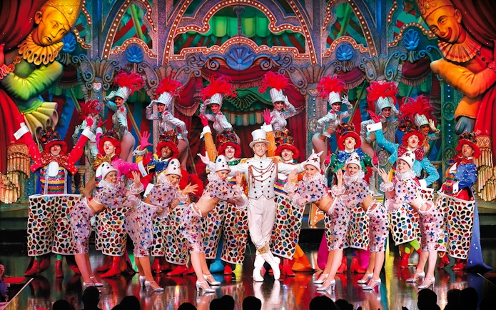 Performers in colorful costumes on stage at the Moulin Rouge Show Féerie, Paris.