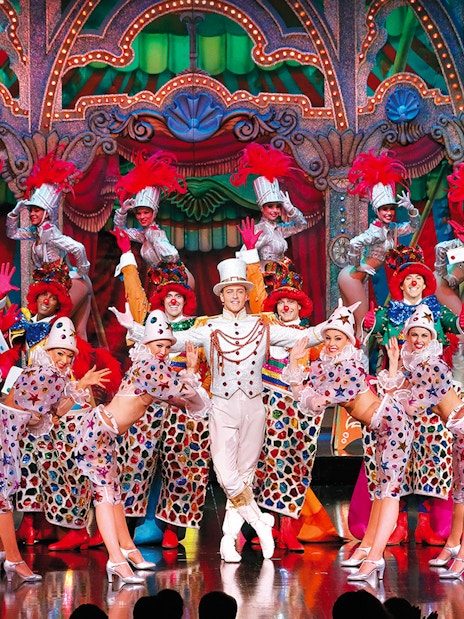 Performers in colorful costumes on stage at the Moulin Rouge Show Féerie, Paris.