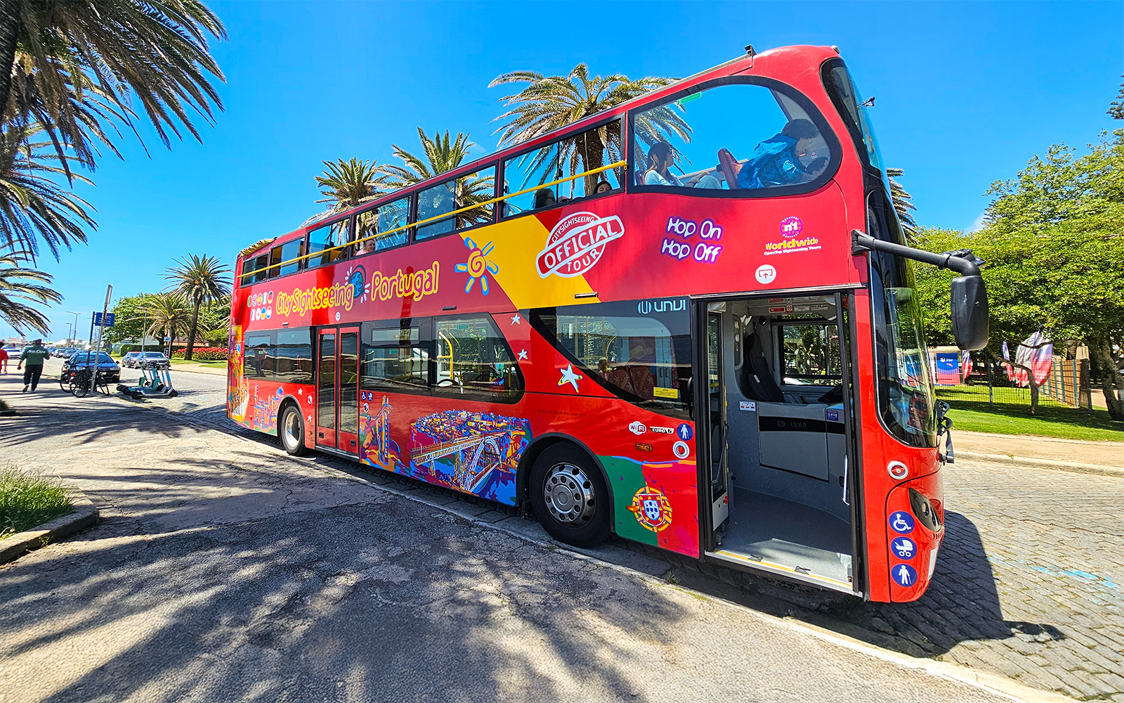 Open-top red sightseeing bus in Porto, Portugal, parked near palm trees.