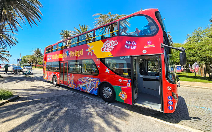 Open-top red sightseeing bus in Porto, Portugal, parked near palm trees.