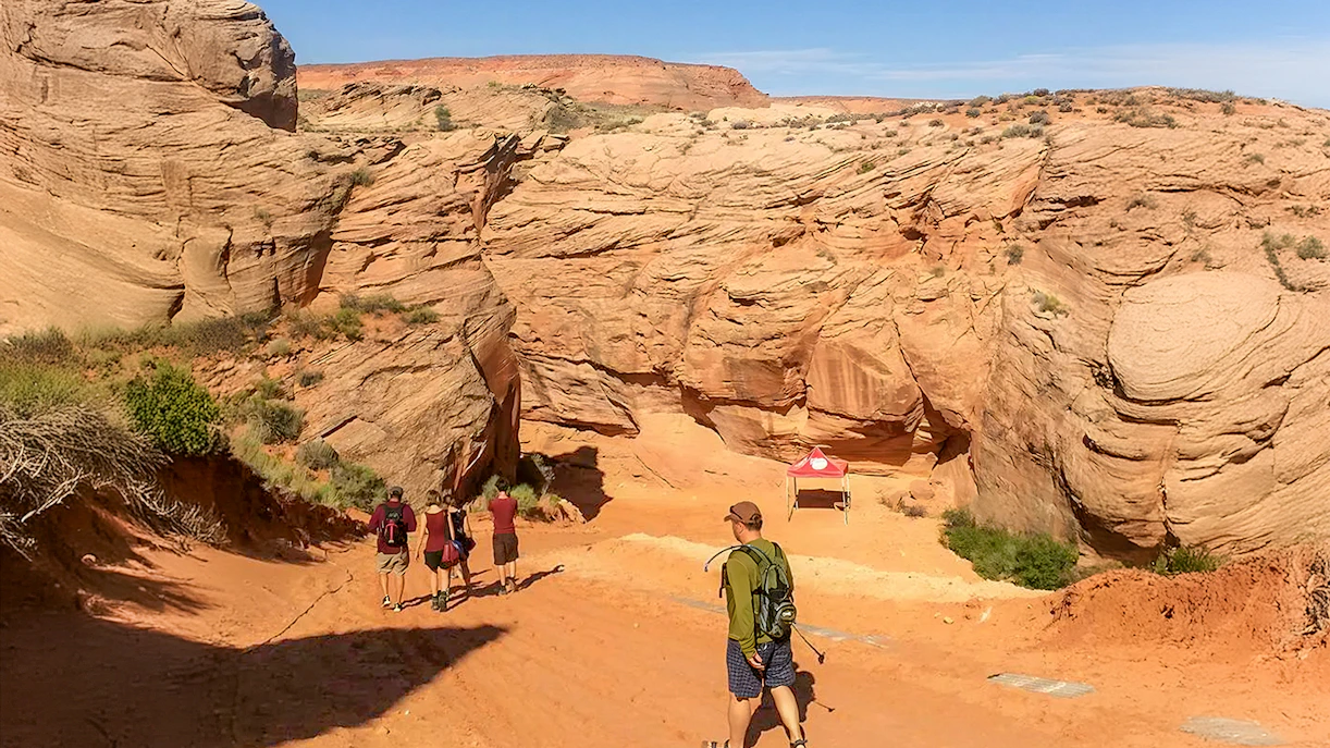 Visitors entering Antelope Canyon X, surrounded by red rock formations in Arizona.