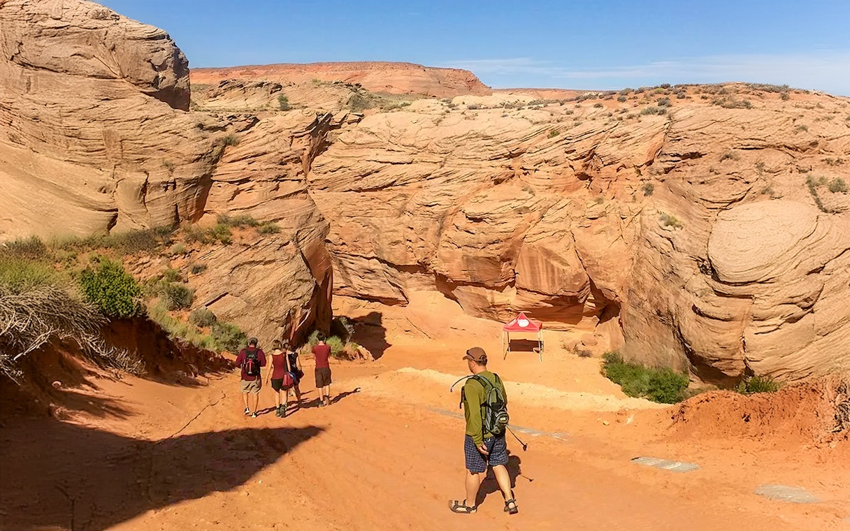 Visitors entering Antelope Canyon X, surrounded by red rock formations in Arizona.
