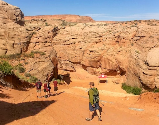 Visitors entering Antelope Canyon X, surrounded by red rock formations in Arizona.
