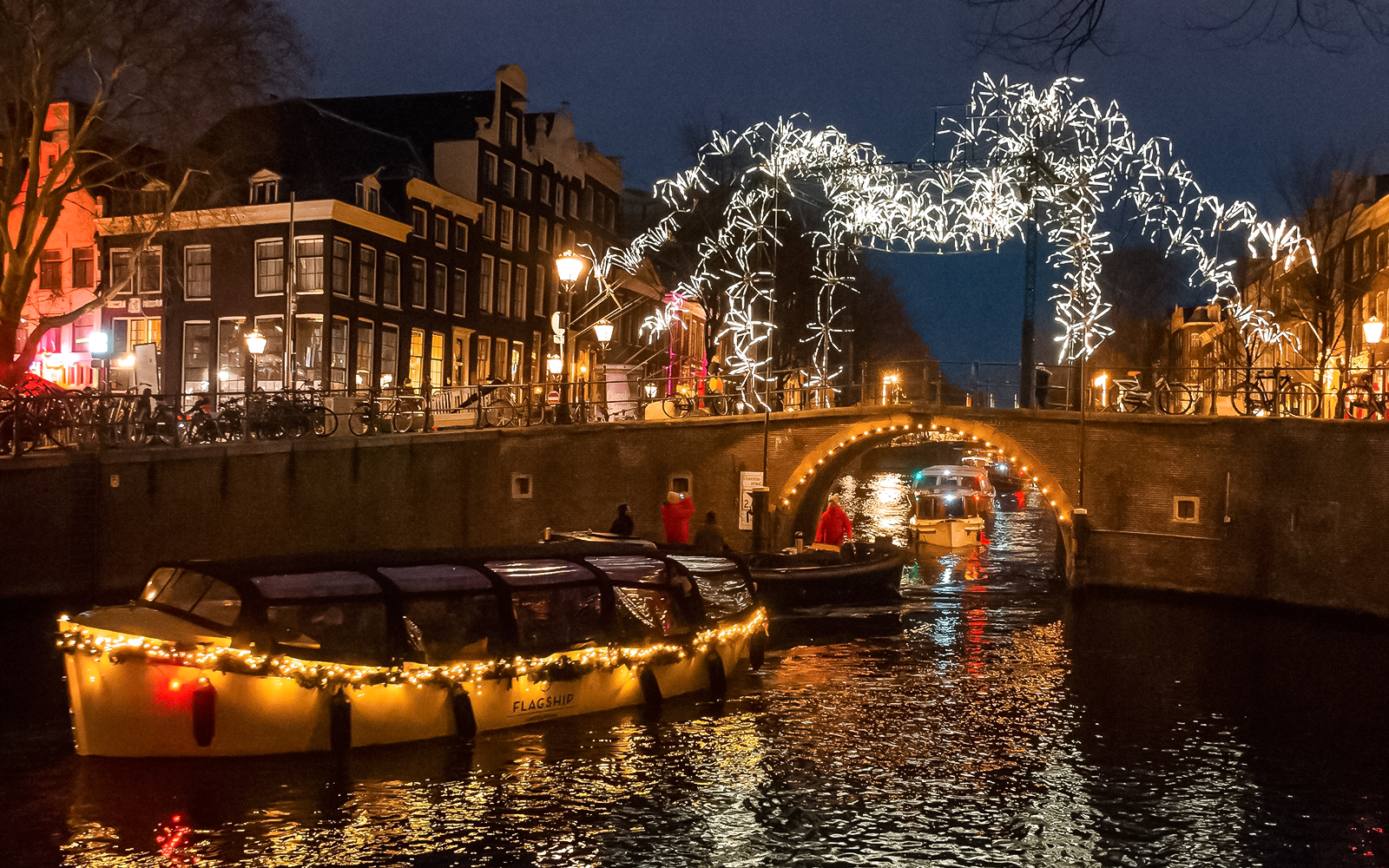 Amsterdam canal cruise during Light Festival with illuminated bridge and buildings.