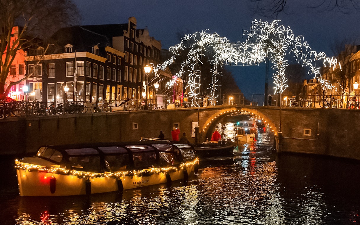 Amsterdam canal cruise during Light Festival with illuminated bridge and buildings.