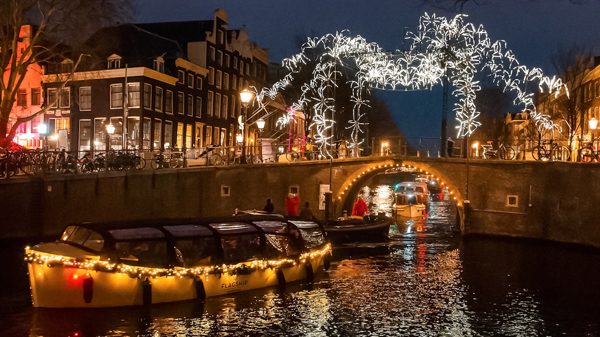 Amsterdam canal cruise during Light Festival with illuminated bridge and buildings.