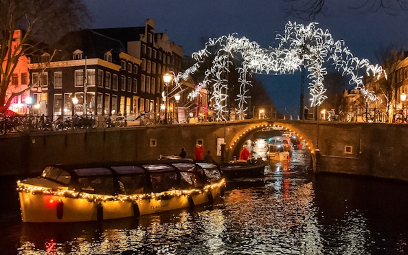 Amsterdam canal cruise during Light Festival with illuminated bridge and buildings.