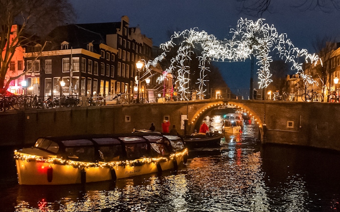 Amsterdam canal cruise during Light Festival with illuminated bridge and buildings.