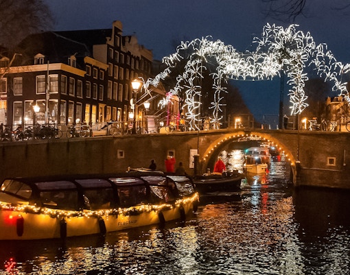 Amsterdam canal cruise during Light Festival with illuminated bridge and buildings.