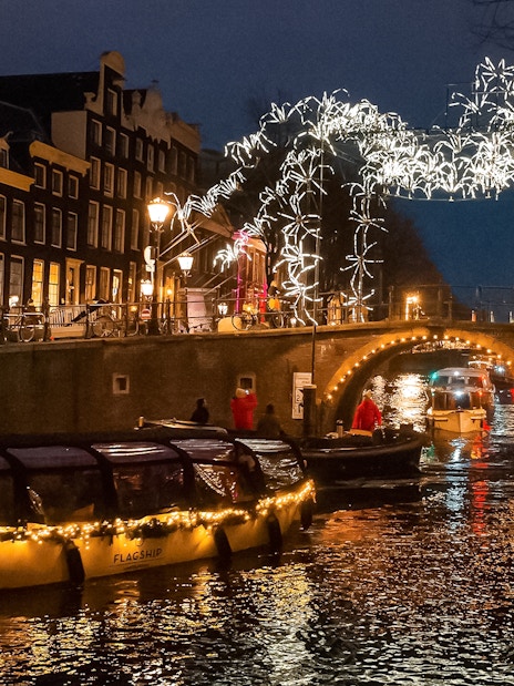Amsterdam canal cruise during Light Festival with illuminated bridge and buildings.