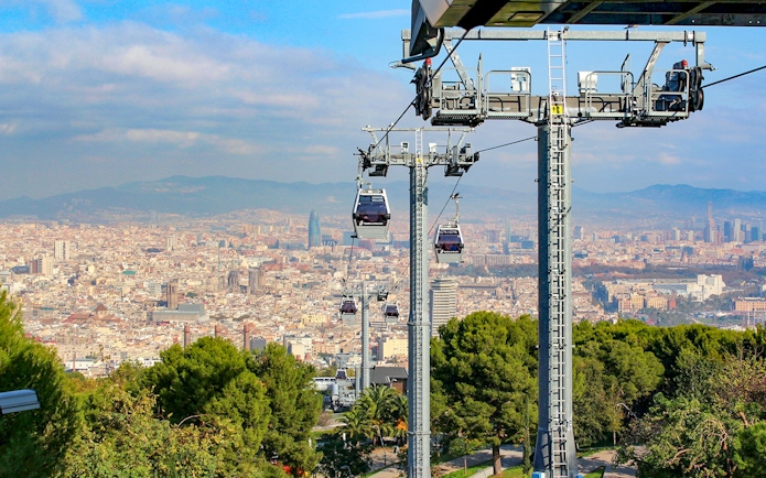 Cable cars ascending Montjuic with Barcelona cityscape in the background.