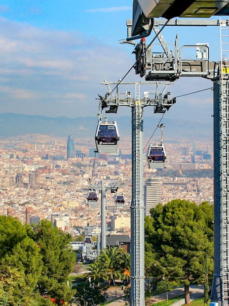 Cable cars ascending Montjuic with Barcelona cityscape in the background.