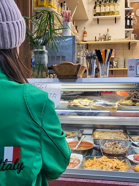 Customer at deli counter during guided food tour in Florence, Italy.