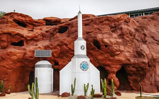 Rocket structure at LOF LAND with red rock backdrop and cacti.