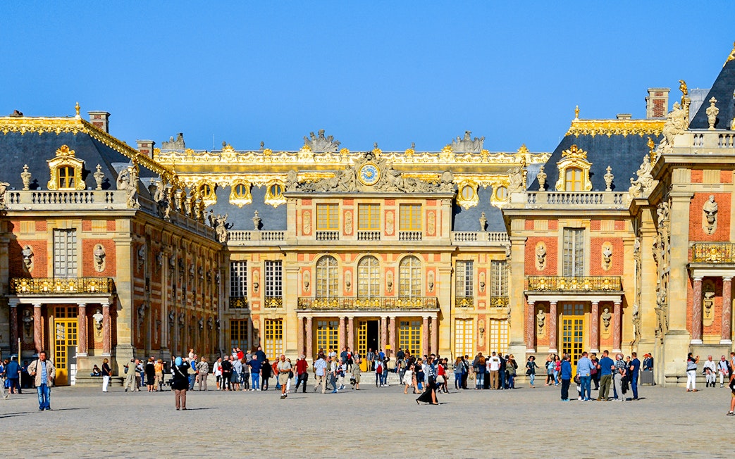 Visitors at the entrance of Versailles Palace, France, with ornate architecture and golden details.