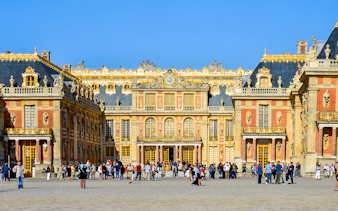Visitors at the entrance of Versailles Palace, France, with ornate architecture and golden details.