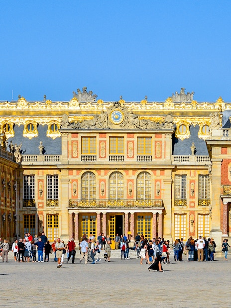 Visitors at the entrance of Versailles Palace, France, with ornate architecture and golden details.
