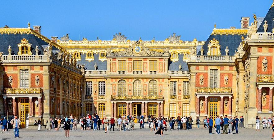 Visitors at the entrance of Versailles Palace, France, with ornate architecture and golden details.