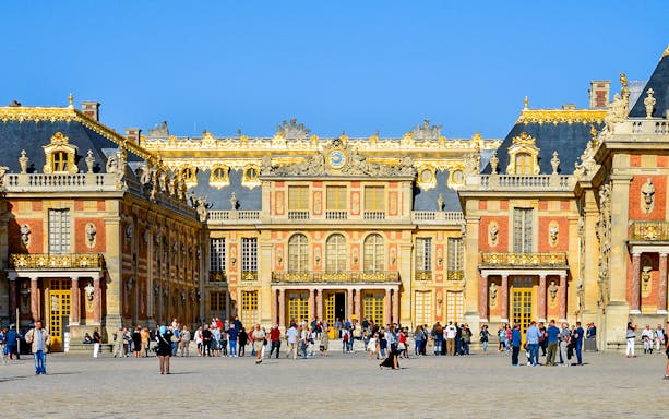 Visitors at the entrance of Versailles Palace, France, with ornate architecture and golden details.