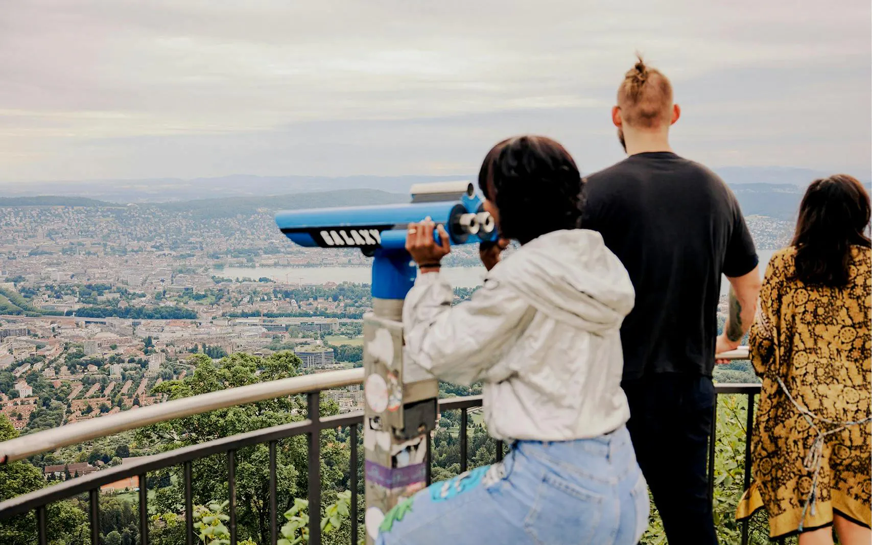 Visitors using a telescope at a Zurich viewpoint overlooking the city.