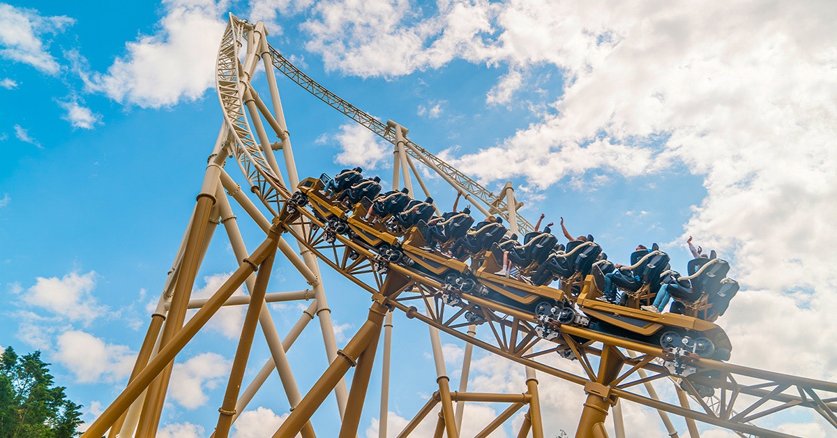 Roller coaster ascending steep track at Thorpe Park, riders with raised hands against blue sky.