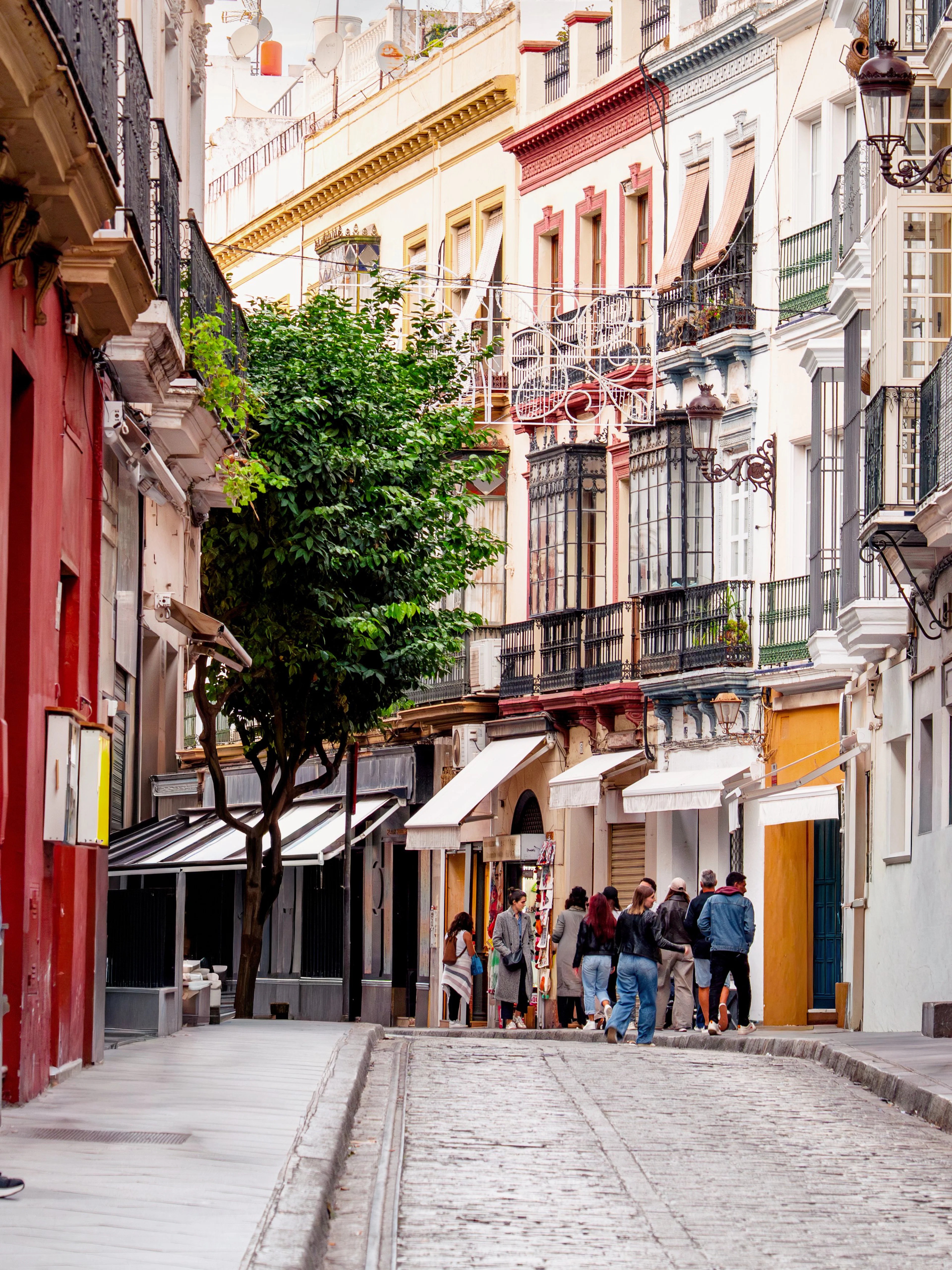 Narrow street in Seville with people walking by cafes and restaurants, Spain.