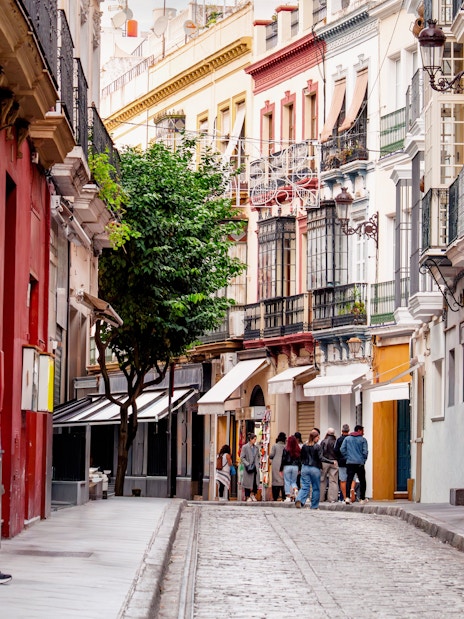 Narrow street in Seville with people walking by cafes and restaurants, Spain.