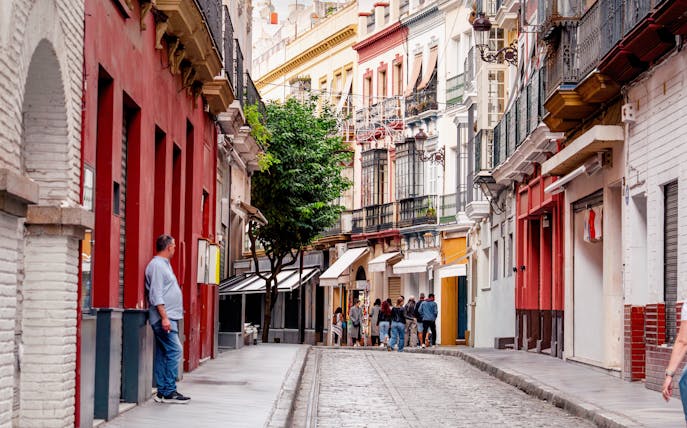 Narrow street in Seville with people walking by cafes and restaurants, Spain.