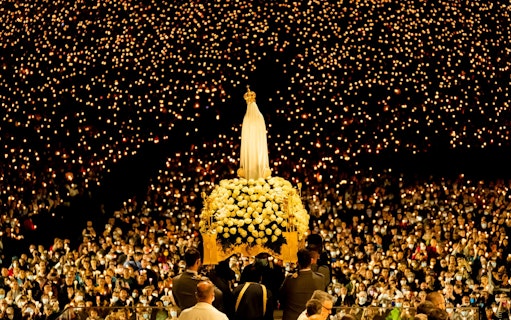 Candlelight procession during Fatima Night Pilgrimage Tour with statue and crowd.