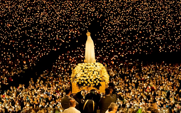 Candlelight procession during Fatima Night Pilgrimage Tour with statue and crowd.