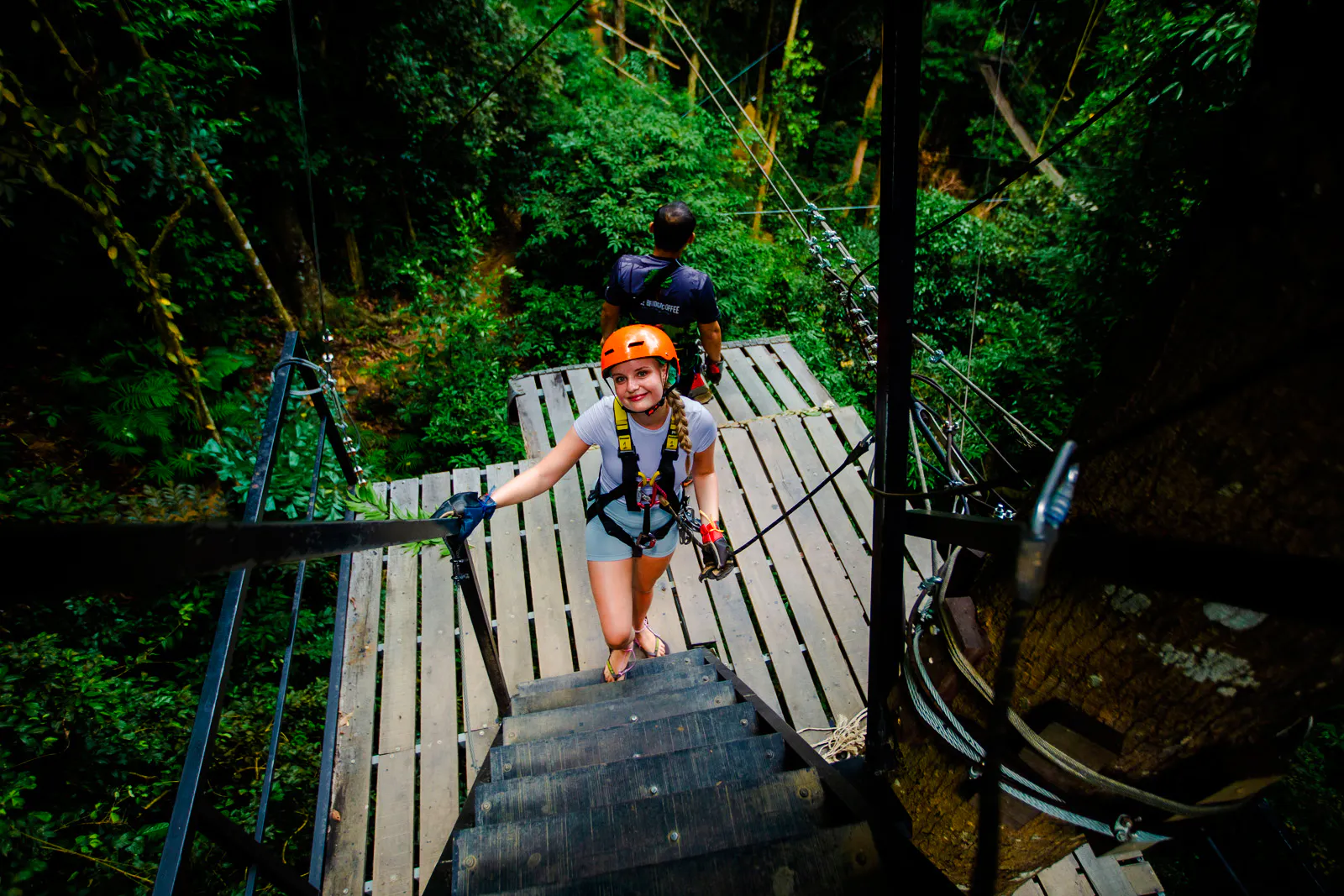 Person on zipline platform in Koh Samui forest, wearing safety gear, ready for Tree Bridge Zipline adventure.