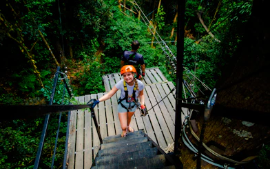 Person on zipline platform in Koh Samui forest, wearing safety gear, ready for Tree Bridge Zipline adventure.